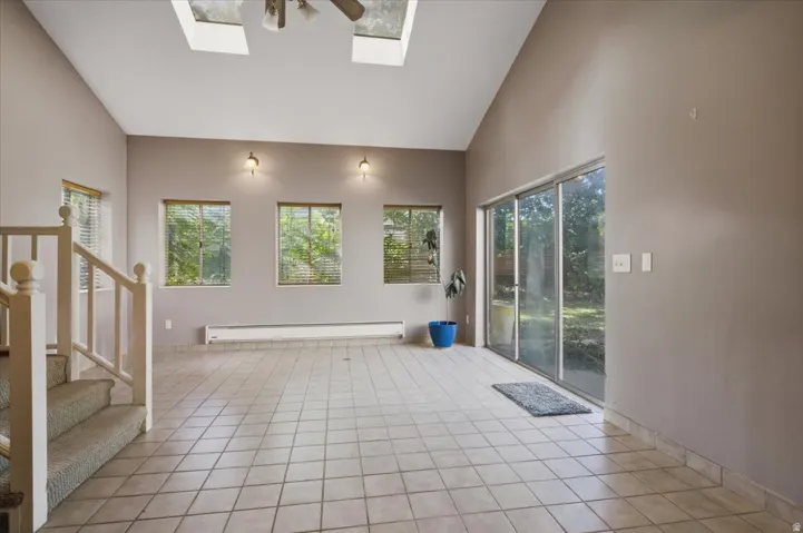 Vaulted ceiling, skylights, ceiling fan, wall sconces, and tile flooring