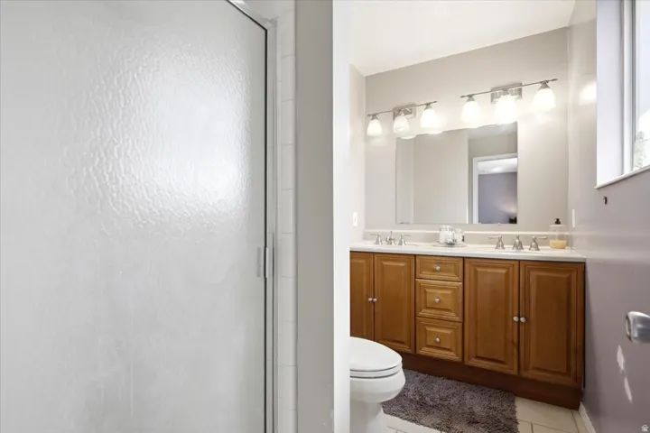 Frosted glass shower enclosure, double vanity with wood-finish cabinetry, dual undermount sinks, and a single mirror with a four-light fixture