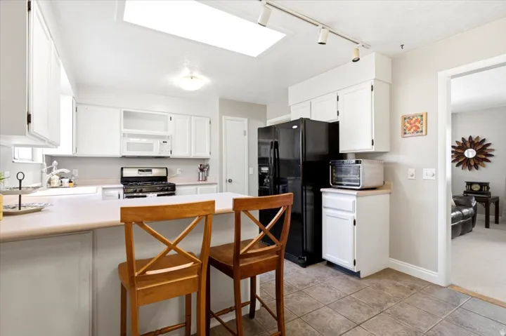 Kitchen featuring white cabinetry, a black refrigerator, a gas range, and a skylight