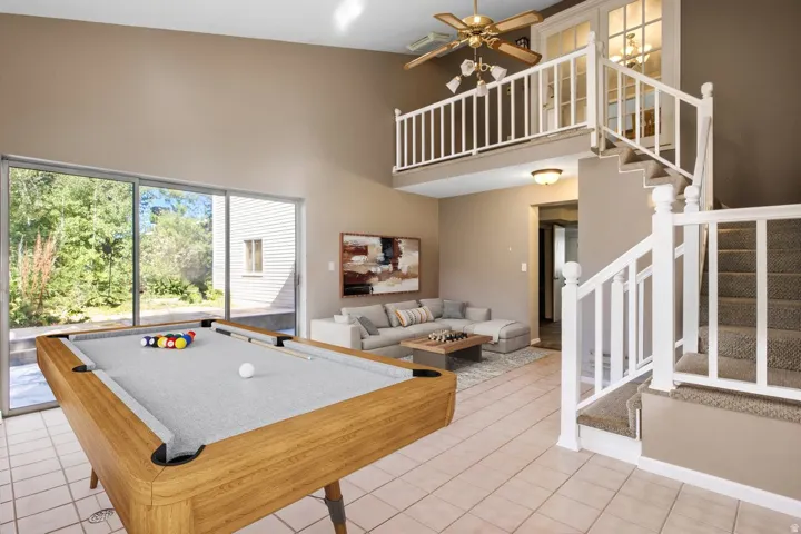 Vaulted ceiling, tiled flooring, sliding glass doors, upper-level landing with French doors, and a carpeted staircase with white railings