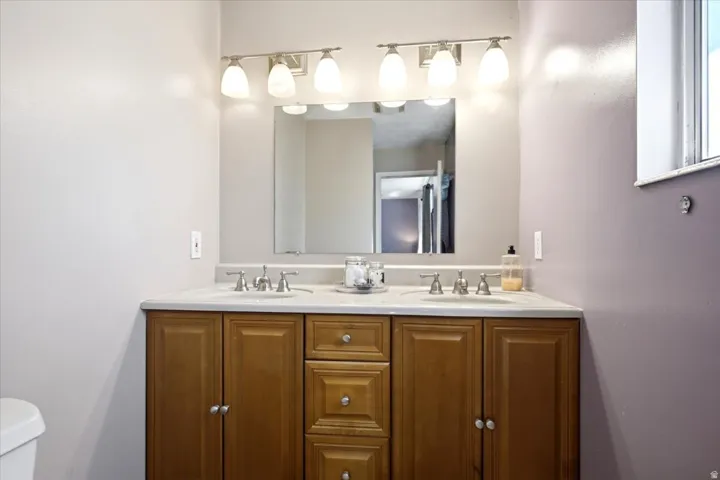 Dual vanity with light wood-finish cabinetry, brushed nickel hardware, and matching light fixtures