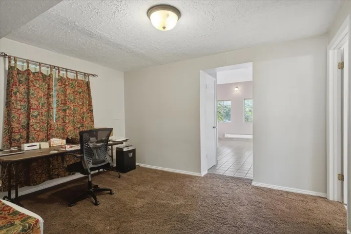 Carpeted room with a ceiling-mounted light fixture and a doorway opening to a tiled area