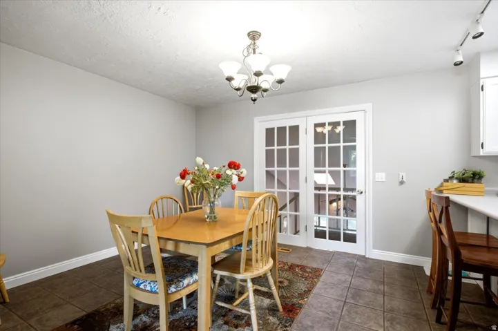 Tile flooring, white French doors, track lighting, ceiling-mounted chandelier, white baseboards