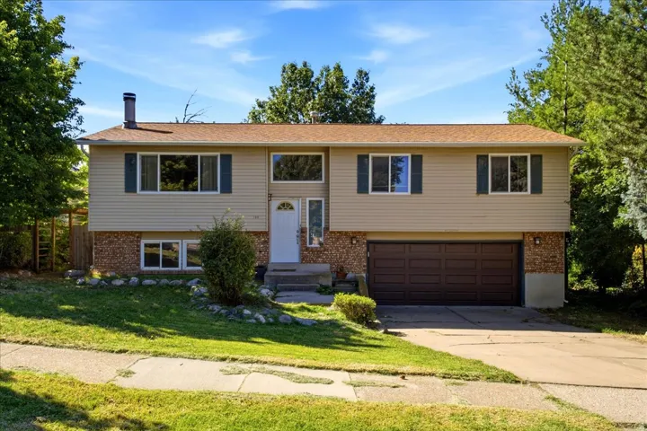 Split-level residence featuring a two-car garage, light-colored siding, and a brown shingle roof