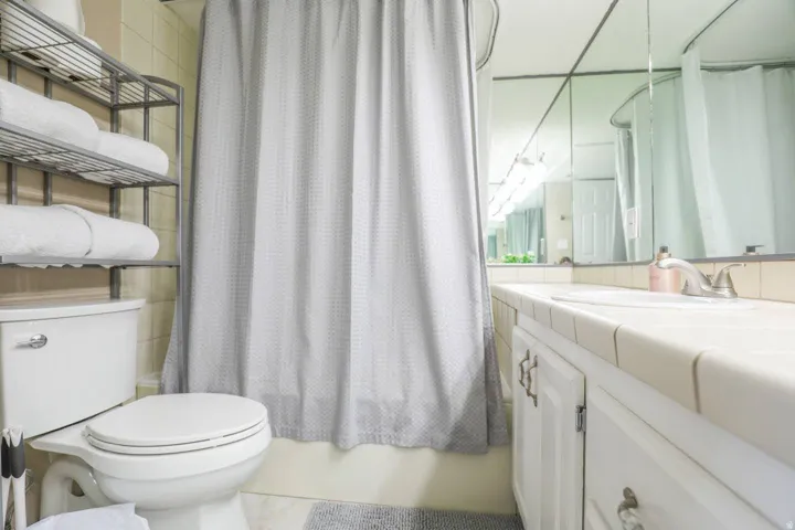 Bathroom featuring a toilet, tile vanity with an integrated sink, white cabinetry with decorative hardware, and a wall-mounted mirror