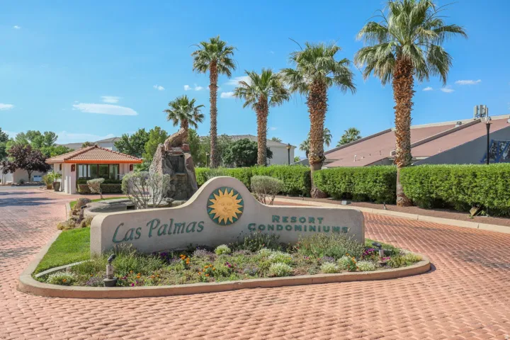 Paver driveway and entrance, lush landscaping, mature palm trees, decorative stone monument sign, and a security kiosk with a tiled roof
