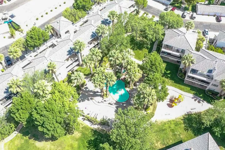 Community pool, playground structure, mature palm trees, manicured green spaces, and multi-unit buildings with tile roofs