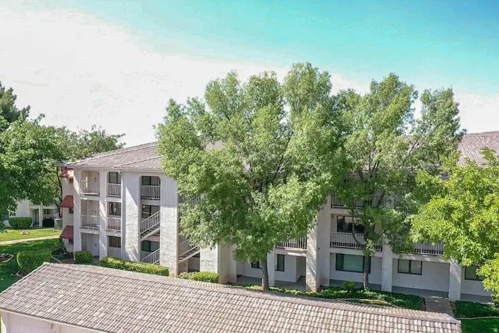 Multi-story building featuring tiled roofing, multiple exterior balconies, external staircases, and surrounding mature trees