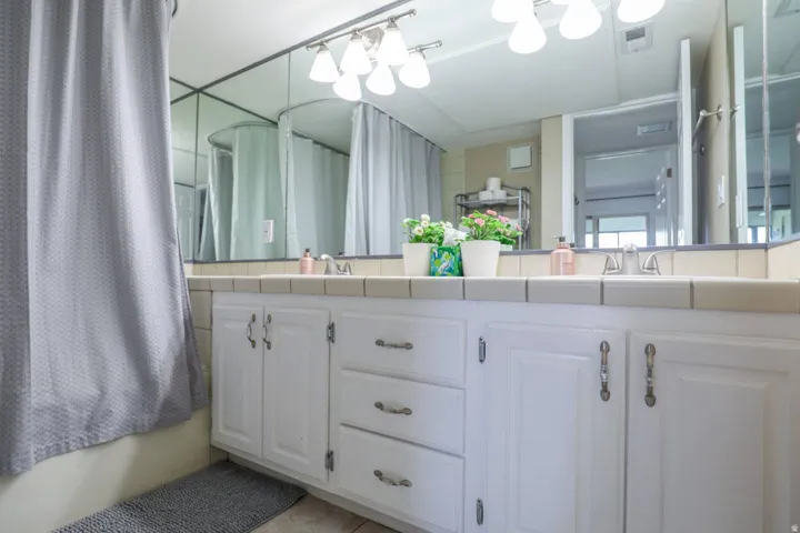 Dual vanity with white cabinetry and chrome hardware, tile countertop, and mirror