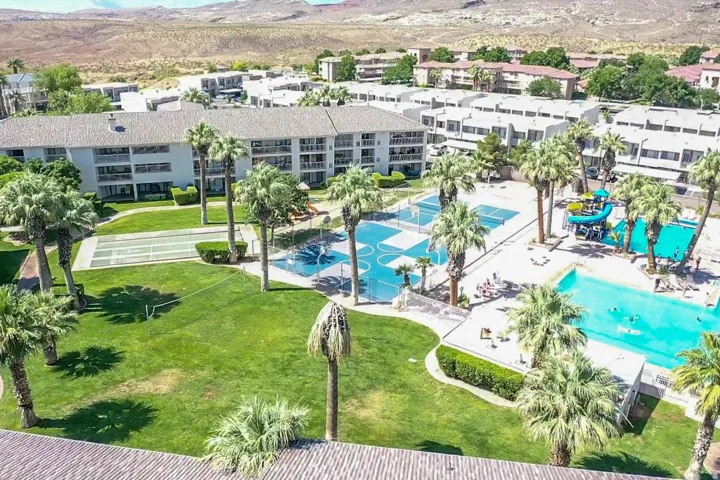 Expansive common area featuring a swimming pool, water slide structure, basketball court, and bocce ball court, surrounded by mature palm trees and green lawns