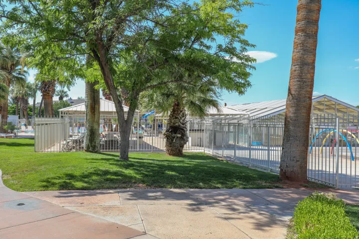 Manicured lawn area with established trees, white metal fencing, and concrete pathways