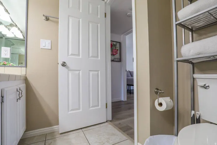 Bathroom with tiled flooring, white vanity cabinetry with decorative pulls, and a built-in toilet storage rack