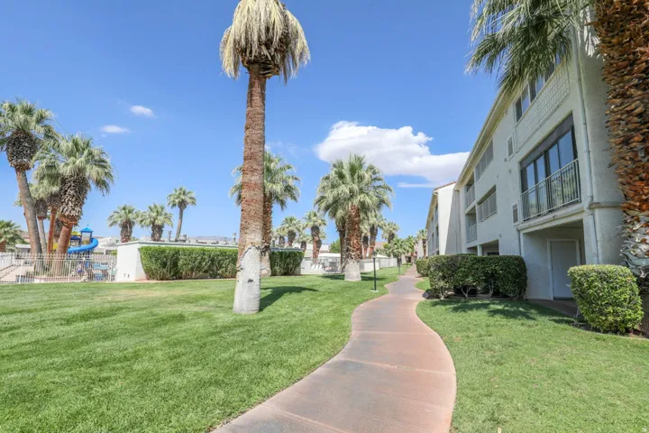 Manicured lawn with mature palm trees, winding paved walkway, and multi-level building with balconies