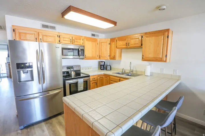Kitchen featuring light wood-finish cabinetry, stainless steel appliances, a tile countertop, and wood-finish flooring