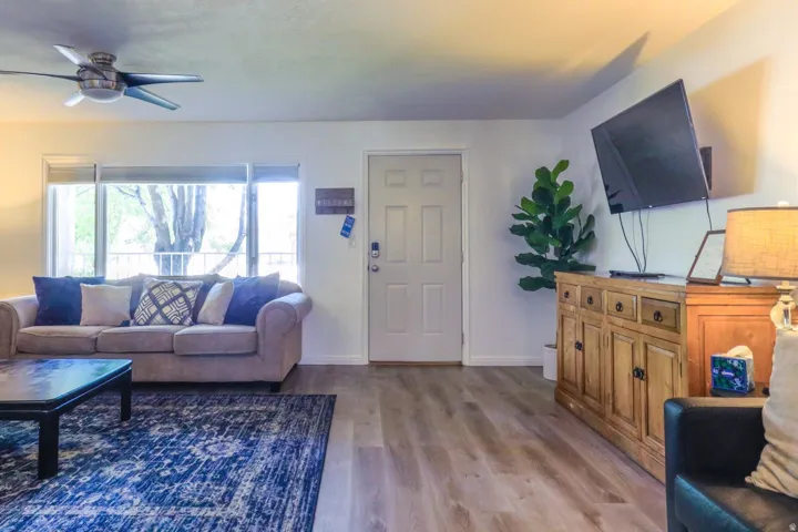 Wood-finish flooring throughout, ceiling fan with integrated lighting, large window providing natural illumination, white panel door