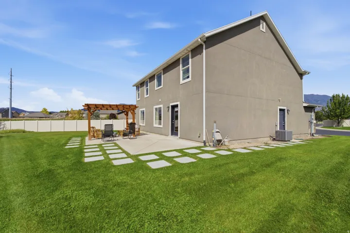 Expansive backyard featuring a large concrete patio, a wood pergola, and a stepping stone pathway