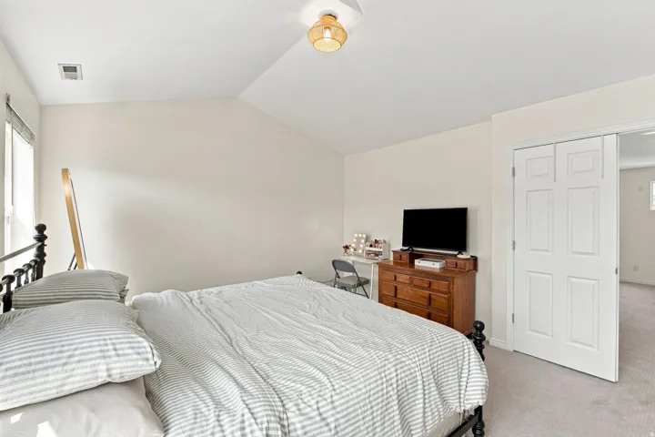 Vaulted ceiling with an attached light fixture, a window with blinds, and white bi-fold doors