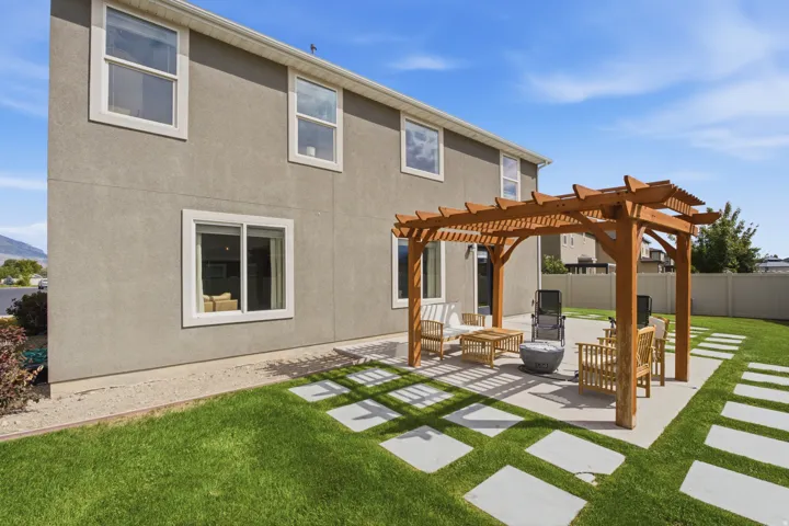 Manicured lawn with a concrete paver pathway, a wooden pergola, and a concrete patio