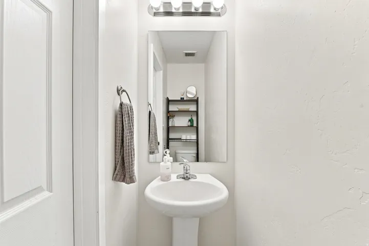 Pedestal sink with chrome faucet, rectangular wall mirror, and vanity light fixture