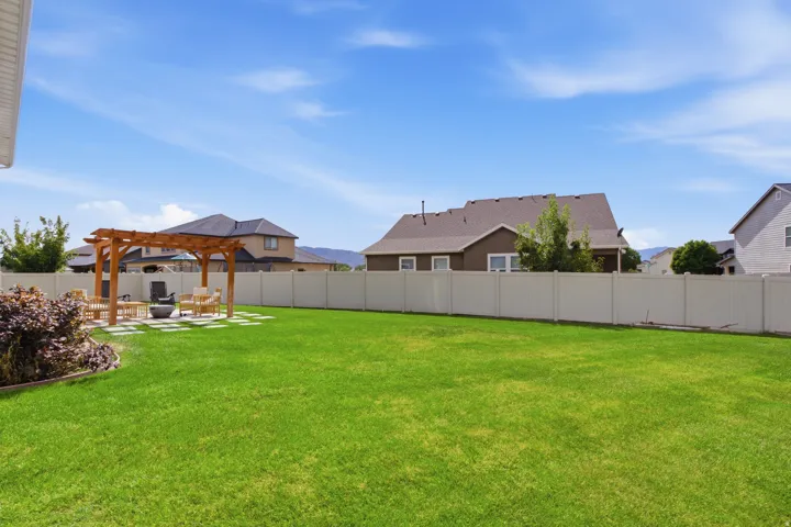 Expansive lawn with a wooden pergola, stone paver patio, and full perimeter fencing