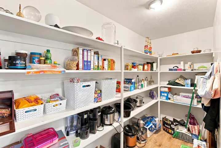 Walk-in pantry with extensive built-in shelving, white walls, and wood-finish flooring