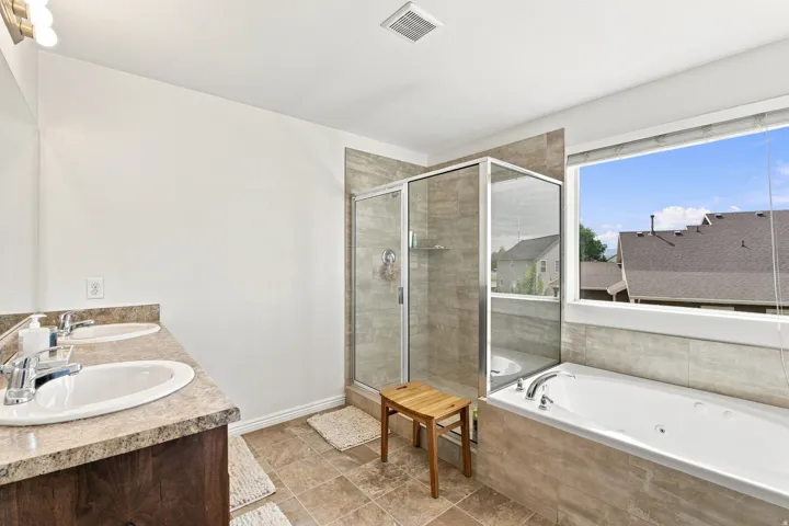 Dual vanity with integrated sinks, tiled walk-in shower, soaking tub, and a large horizontal window