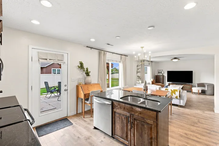 Open concept living area with wood-finish flooring, recessed lighting, and a kitchen island featuring a dual basin sink