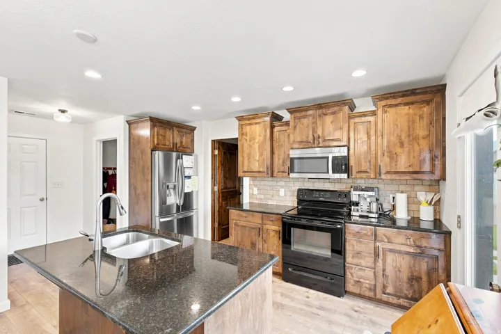 Kitchen featuring wood-finish cabinetry, dark countertops, stainless steel appliances, and a tile backsplash