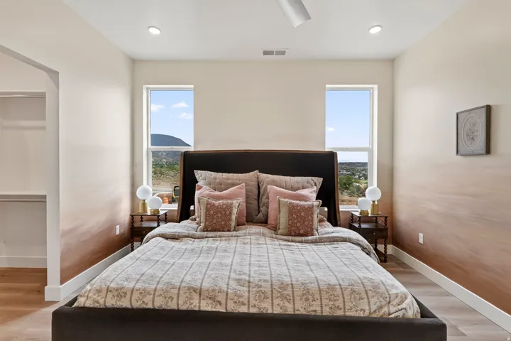 Recessed ceiling lighting, wood-finish flooring, two large windows, open closet with shelving, and a ceiling fan
