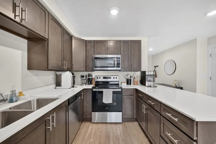 U-shaped kitchen with wood-finish cabinetry, stainless steel appliances, dual basin sink, and ample countertop space