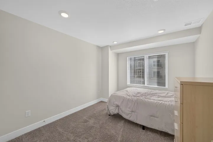 Recessed ceiling lighting with a neutral wall color, carpeted flooring, and a large window with blinds