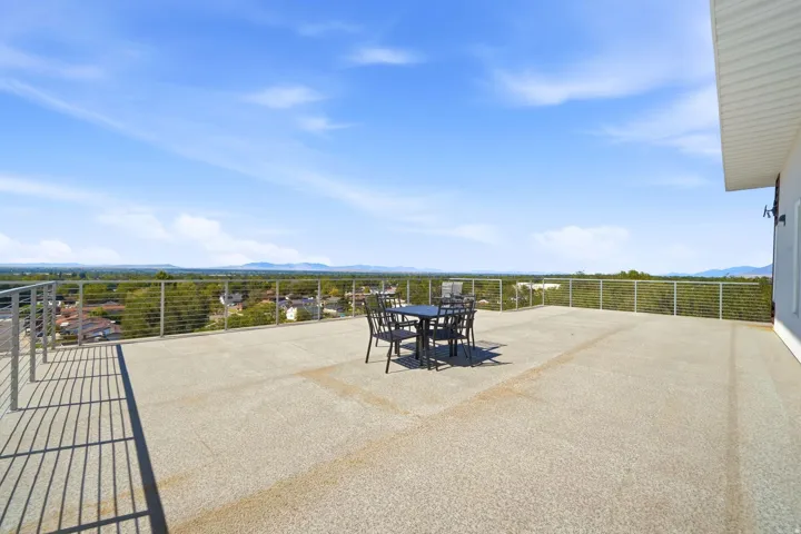 Expansive rooftop terrace featuring a textured floor, modern cable railings, and a wide-ranging distant landscape