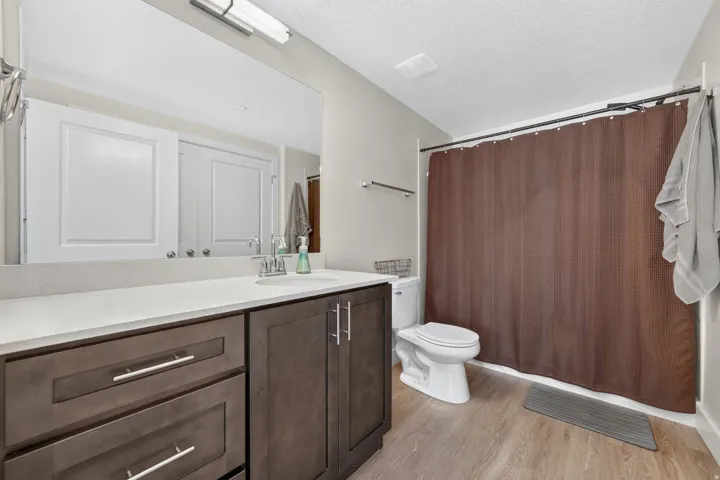 Contemporary vanity with a white countertop and integrated sink, dark wood-finish cabinetry, chrome hardware, and wood-finish flooring