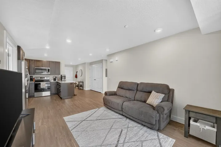 Open-concept living area featuring wood-finish flooring, recessed lighting, and a kitchen with stainless steel appliances, dark cabinetry, and an island