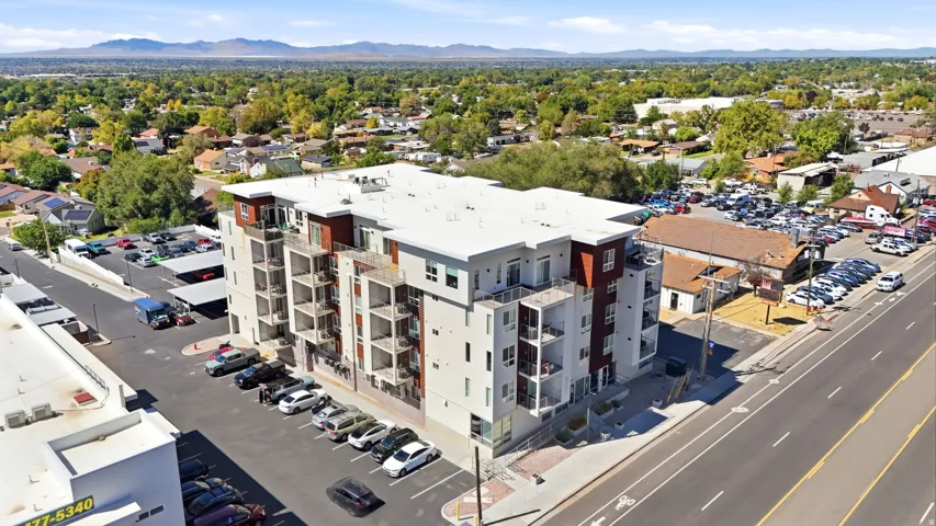 Modern multi-story building featuring exterior balconies, a dedicated parking lot, and covered parking structures