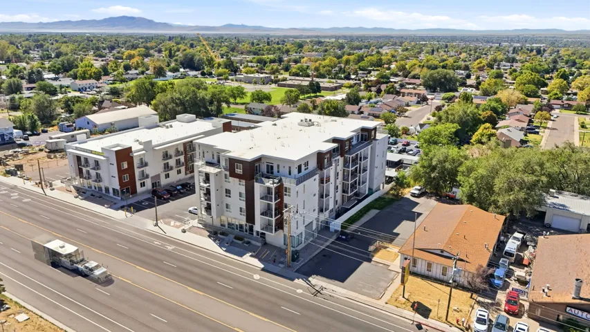 Modern multi-story building featuring multiple balconies, a flat roof, and a paved parking area