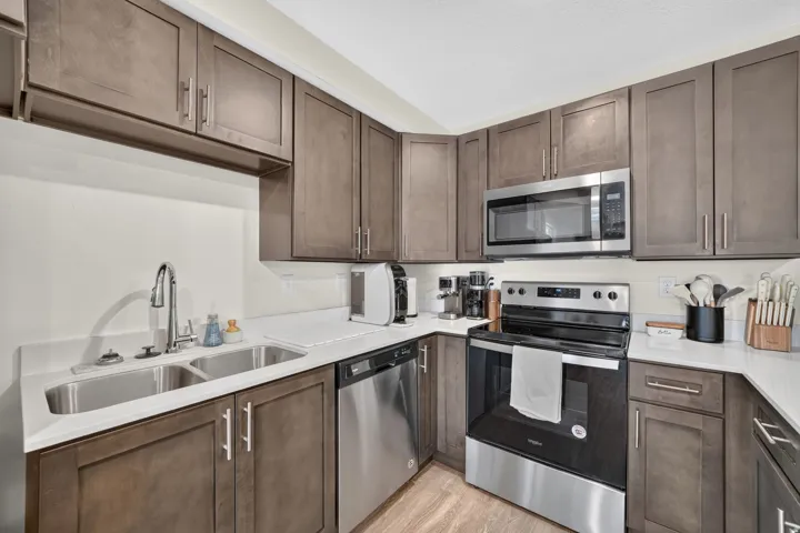 Kitchen featuring rich wood cabinetry, stainless steel appliances, a double basin sink with a high-arc faucet, and light-toned countertops