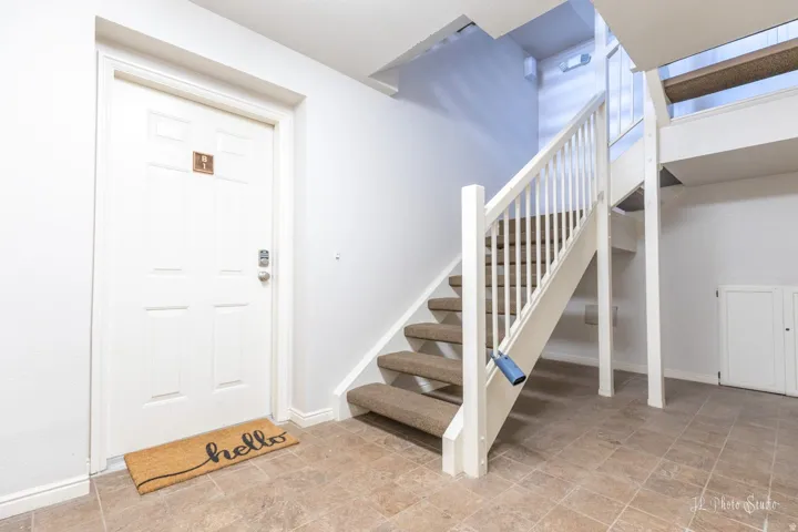 Panel door with a smart lock, tiled flooring, and carpeted stairs with a white railing