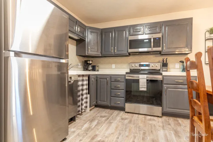 Stainless steel appliances, wood-finish flooring, white countertops, gray cabinetry, and a tile backsplash