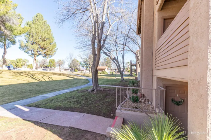 Exterior stucco finish, private balcony, ground-level entry, mature trees, and a concrete pathway