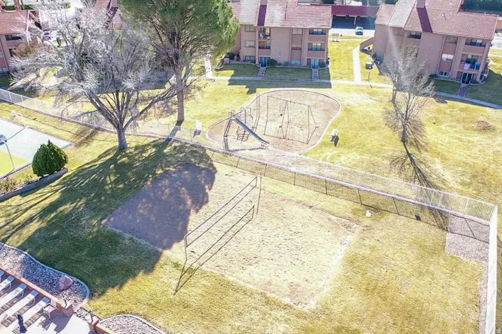 Grassed recreational area with a sand volleyball court, playground equipment, and a hard-surface court