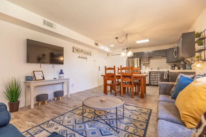 Open-concept living space featuring wood-finish flooring, a dining area with a wooden table and chairs, and a kitchen with dark cabinetry and stainless steel appliances