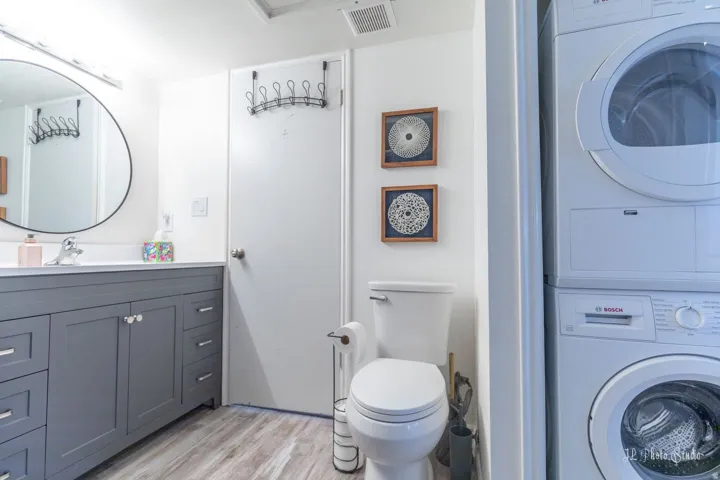 Contemporary bathroom featuring a gray vanity with a white countertop, round wall-mounted mirror, and wood-finish flooring