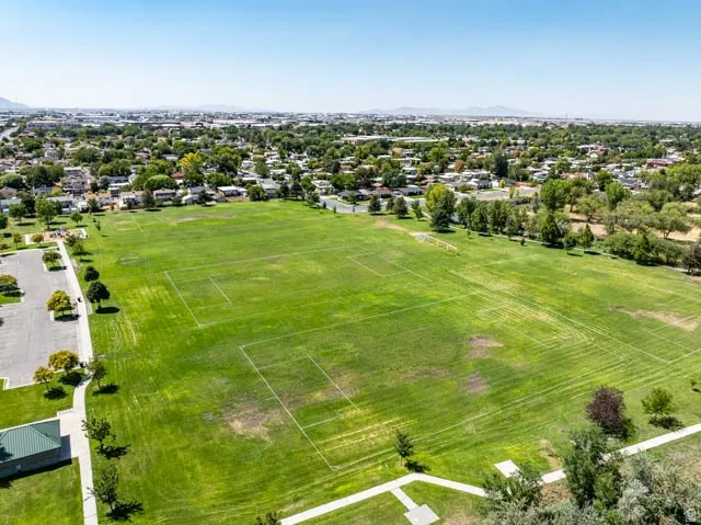 Expansive green field featuring multiple marked sports areas, bordered by a paved parking area and mature trees