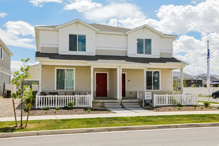Two-story residence featuring light-colored siding, a covered front porch, and a white picket fence enclosing a patio area