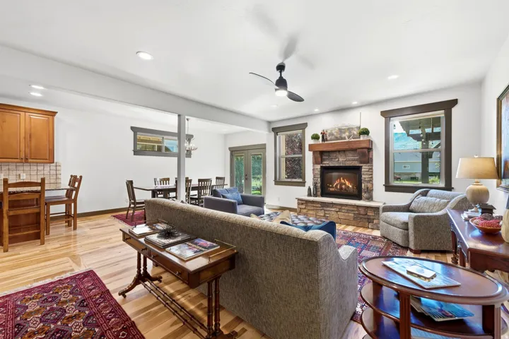 Hardwood-finish flooring throughout, integrated kitchen cabinetry, stone-clad fireplace with wood mantel, ceiling fan, and recessed lighting