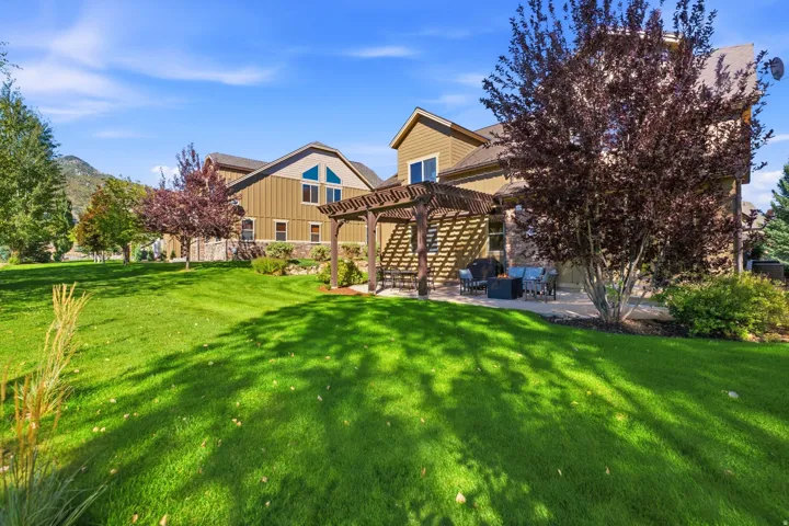 Expansive green lawn, stone patio with pergola, multi-story exterior with siding and stone accents, mature trees