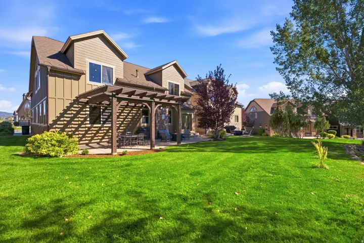 Expansive backyard featuring a manicured lawn, established pergola, and patio space