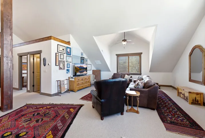 Expansive room with sloped ceilings, carpeted flooring, exposed wooden support beam, and a ceiling fan with integrated lighting