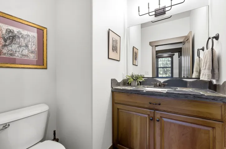 Vanity featuring a dark stone countertop, integrated sink, and wood-finish cabinetry with dark hardware